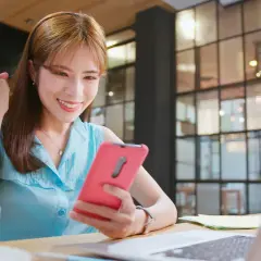 Uśmiechnięta kobieta sprawdza telefon, zastanawiając się, czy zarabianie na grach jest legalne. Sukces w grach online może być realny!