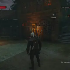 Geralt stoi przed kamienną budowlą, gdzie czeka go serce z kamienia zakończenia misji. W tle widać strażnika z pochodnią.