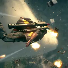 Rico z Just Cause 5 w akcji, lecący w powietrzu z wyrzutnią rakiet, otoczony eksplozjami i spadającymi obiektami.