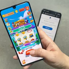 Gra Coin Master na telefonie, pokazująca zarabianie na grach. W tle ekran logowania do PayPal.