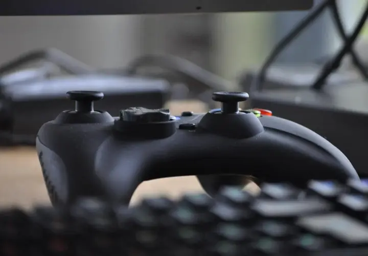 Czarny kontroler do gier leży na klawiaturze, gotowy do akcji. W tle widać monitor, jakby tworzył **steam cloud** dla wirtualnych światów.