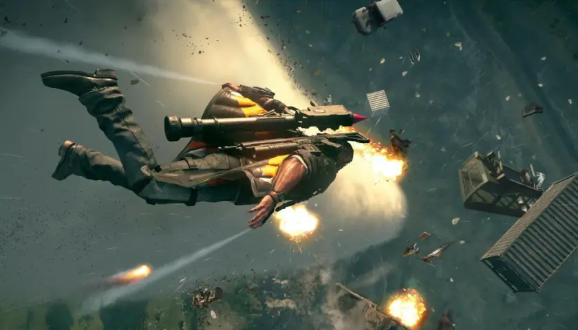 Rico z Just Cause 5 w akcji, lecący w powietrzu z wyrzutnią rakiet, otoczony eksplozjami i spadającymi obiektami.