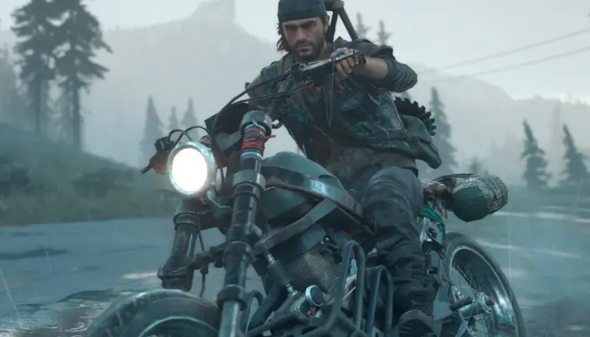 Mężczyzna w czapce i kamizelce jedzie motocyklem w deszczu, w tle las i góry. To scena z gry Days Gone 2.
