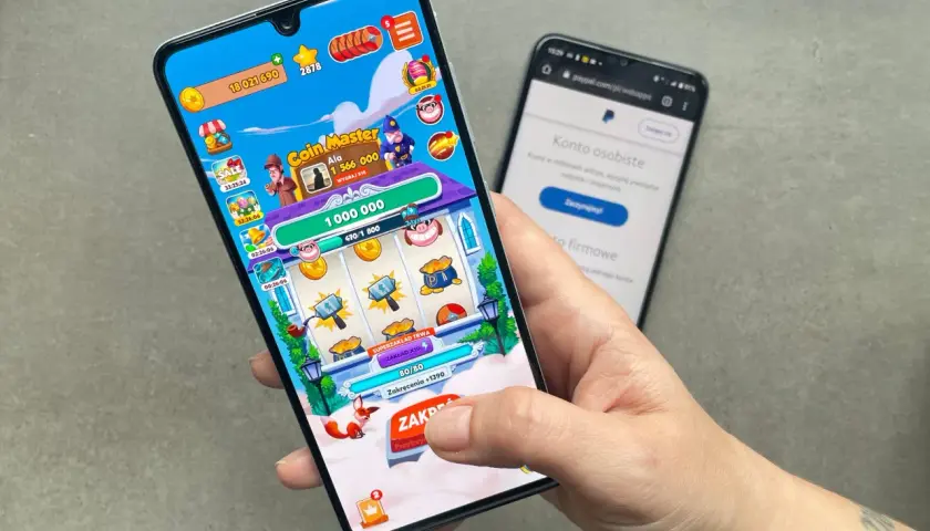 Gra Coin Master na telefonie, pokazująca zarabianie na grach. W tle ekran logowania do PayPal.