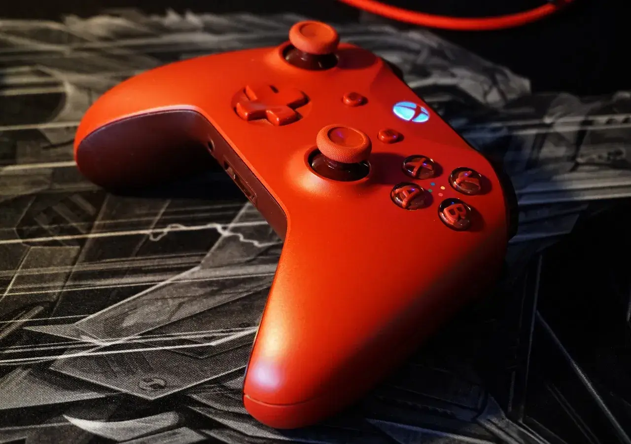 Czerwony kontroler Xbox na czarnej podkładce z motywem graficznym. Idealny do gry z nowym dlc.
