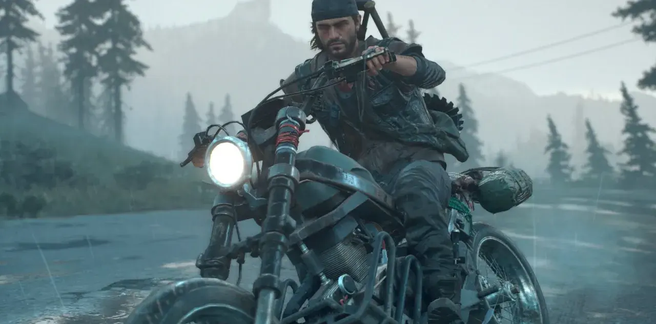 Mężczyzna w czapce i kamizelce jedzie motocyklem w deszczu, w tle las i góry. To scena z gry Days Gone 2.