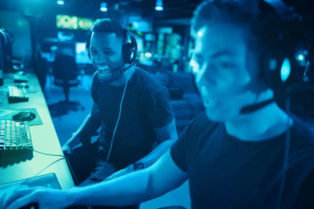 Dwóch graczy w słuchawkach śmieje się podczas emocjonujących gier multiplayer.